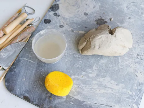 Ton, Töpferwerkzeug, eine Schale mit Wasser und ein gelber Schwamm liegen auf einem Tisch.