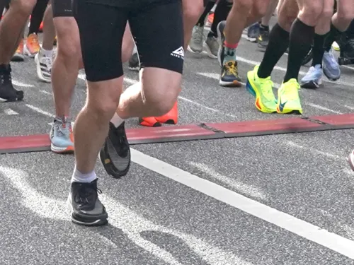 Ausschnitt von Menschen, die auf Asphalt in Sportsachen und Laufschuhen laufen, zu sehen sind die Beine und Füße.