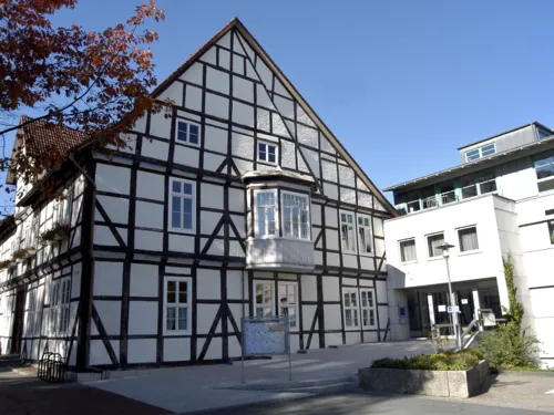 Fachwerkhaus mit weißen Fenstern und einem weißen Erker im ersten OG. Rechts am Fachwerkhaus befindet sich ein moderner Anbau in Kubusform.