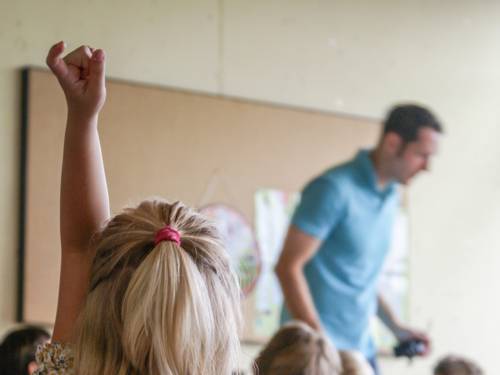 Eine Schülerin zeigt auf, im Hintergrund steht ein Lehrer.