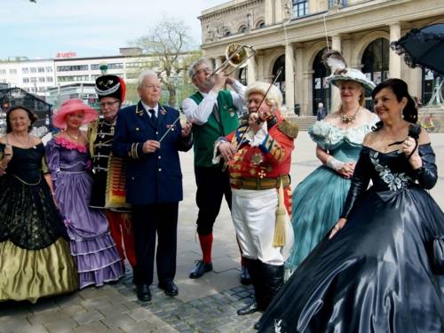 Vier Männer und vier Frauen in historischen Kostümen vor einem Gebäude.