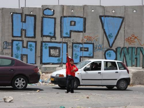 Eine Mauer, auf der in großen Buchstaben Hip Hop steht. Davor ein Junge, der einen Arm in die Höhe streckt
