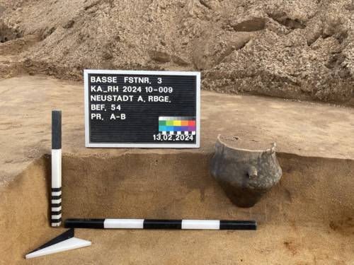 Teilweise freigelegte Urne aus der Bronzezeit. Die aufrecht stehende Urne befindet sich hälftig noch im Sand einer Baugrube.