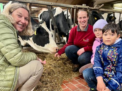Zwei Frauen und zwei Kinder schauen in die Kamera, die vier Personen sind in einem Stall mit Kühen.