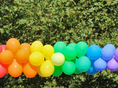 Luftballons sind draußen bei einer Veranstaltung so aufgehängt, dass sie einen Farbverlauf wie bei einem Regenbogen bilden.