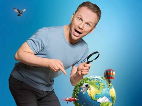 Der Komiker Ralf Schmitz hält eine Lupe in der Hand und betrachtet damit von oben die Erdkugel.