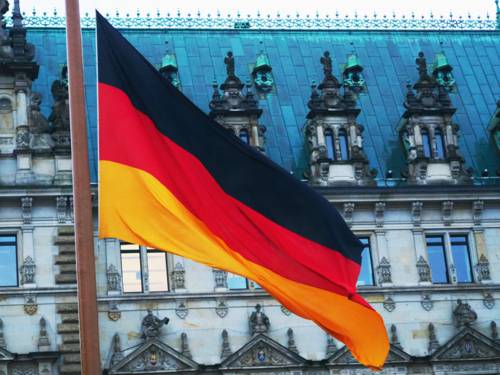 Eine Flagge in den Farben Schwarz, Rot und Gold weht im Wind vor einem historischen Gebäude.
