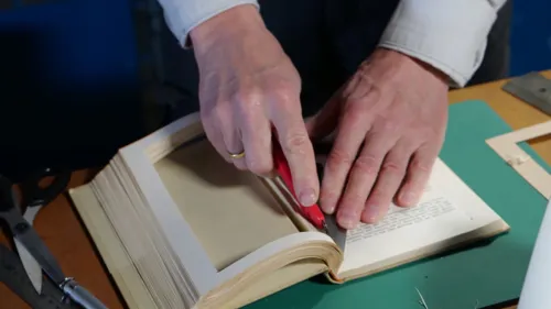 Eine Person schneidet Seiten aus einem Buch aus.