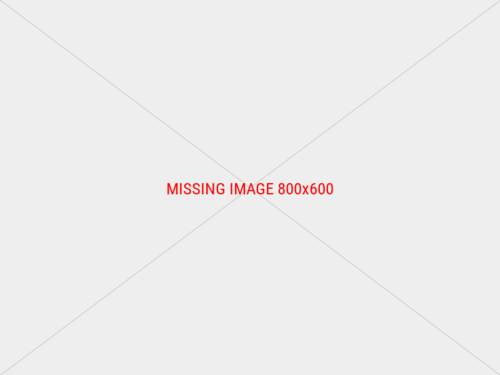 Ein kleiner Holzsteg, auf dem zwei Gläser mit einer Kerze drin stehen. Vom Steg aus hat man Blick auf das Wasser und am beleuchteten Ufer sind Menschen zu sehen.