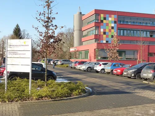 Blick vorbei an einem Schild und parkenden Autos auf ein Schulgebäude.