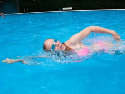 Eine Frau mit Schwimmbrille krault im Freibad durch das Becken