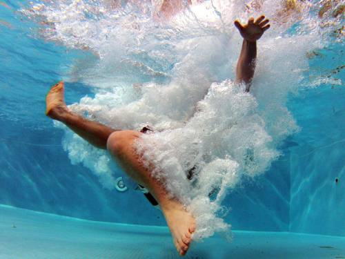 Unterwasserfoto von einer männlichen Person nach einem Sprung ins Wasser, die Person ist nahezu ganz in eine Wolke aus Luftblasen gehüllt