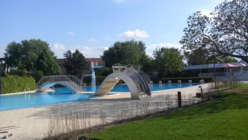 Das mit Wasser gefüllte Aussenbecken des Hallenfreibades Burgdorf ohne Badegäste bei schönem Wetter mit breiter Spaßrutsche, Sprungturm und Brücke