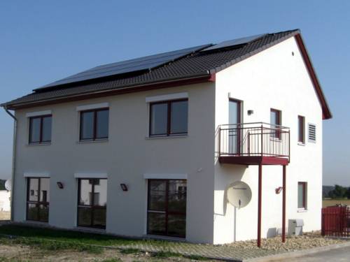 Einfamilienhaus mit weißer Fassade, großen Fenstern und einem Balkon. Auf dem Dach ist eine Solaranlage, Photovoltaikzellen erzeugen Strom, Solarthermie sorgt für Wärme.
