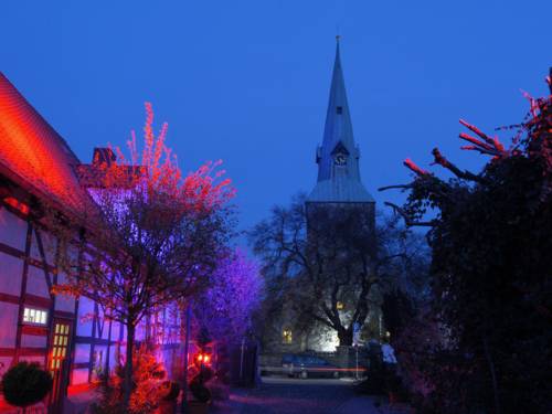 Ein Fachwerkgebäude wird von Scheinwerfern angestrahlt und leuchtet in Farbtönen von Rot bis Violett. Im Hintergrund ragt der Turm der St. Andreas-Kirche in den Nachthimmel.