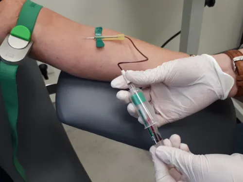 Der Arm einer Person mit einem Stauschlauch, Blut fließt über die Kanüle in das Abnahmeröhrchen.