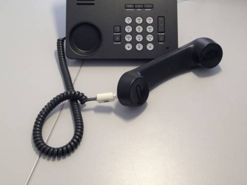 Ein schwarzes Telefon mit Tastatur, bei dem der Hörer abgenommen wurde und davor liegt.