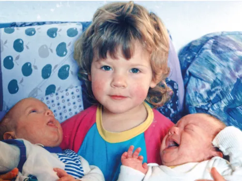 Kleineres Kind mit zwei Babies links und rechts im Arm