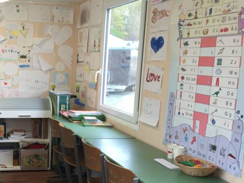 Der Schulwagen von Innen mit Tischen und Stühlen. Die Wände sind beklebt mit Zeichnungen, Bastelarbeiten und Unterrichtsmaterialien.  