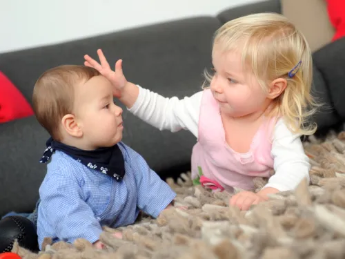 Zwei kleine Kinder auf einem Teppich beim Spielen 