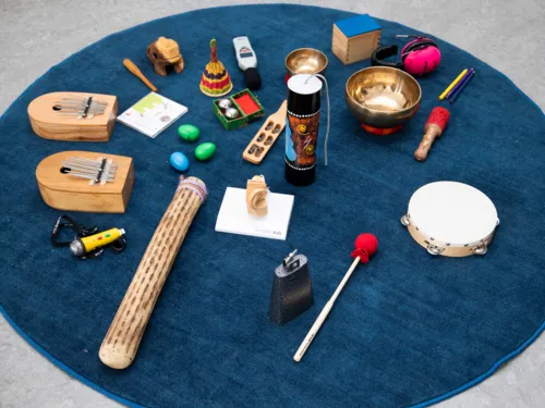 Musikinstrumente, Alltagsgegenstände, Gehörschutz und ein Lautstärkemessgerät liegen auf einem Teppich.