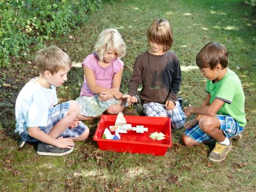 Vier Kinder im Garten lassen Papierspielzeug in einer Wanne schwimmen