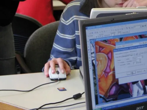 Blick auf einen eingeschaltete Computermonitor und Personen im Raum.