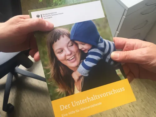 Eine Person übergibt einer anderen eine Broschüre. Es sind lediglich die Hände zu sehen.