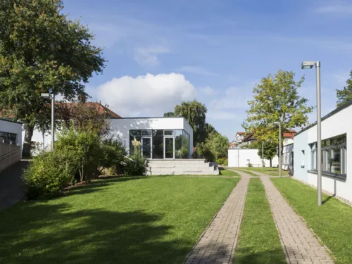 Mehrere kleine, weiß verputzte Häuser mit Flachdach und dazwischen grüne Rasenfläche. Auf dem Gelände befinden sich außerdem mehrere Bäume und Straßenlaternen.