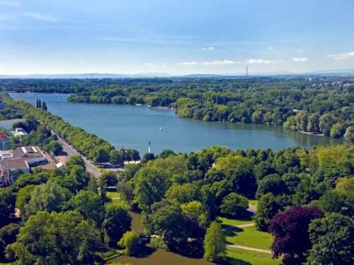 Die Wasserfläche des Maschsees ist von grünen Bäumen umgeben, der Himmel leuchtet blau.