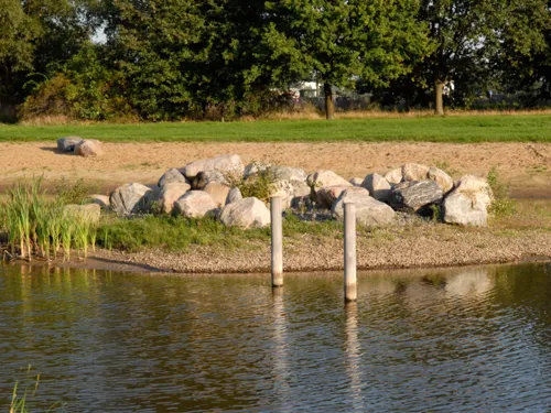 Blick über Wasser auf Feldsteine und Sandstrand