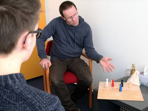 Ein Mann analysiert mit einem Jugendlichen mithilfe von Spielfiguren, welche Position bestimmte Personen zueinander einnehmen.