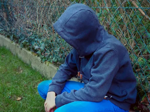 Ein Jugendlicher hockt vor einem Maschendrahtzaun.
