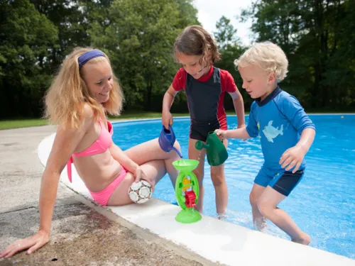 Zwei Kinder mit ihrer Mutter am Rand eines Kinderbeckens im Freibad, die Kinder tragen zum Schutz vor der Sonne spezielle T-Shirts