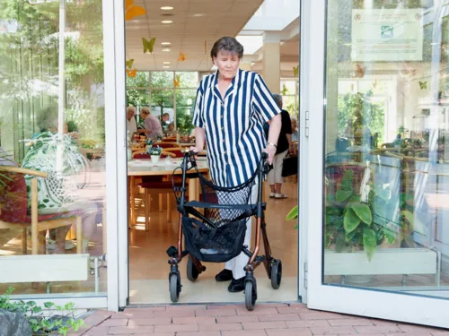 Eine ältere Frau schiebt einen Rollator durch eine Terrassentür.