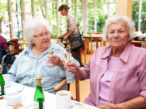 Zwei Seniorinnen stoßen mit einem Getränk an.