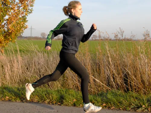 Eine Frau läuft auf einem geteerten Feldweg, kein Fuß berührt im Moment der Aufnahme den Boden.