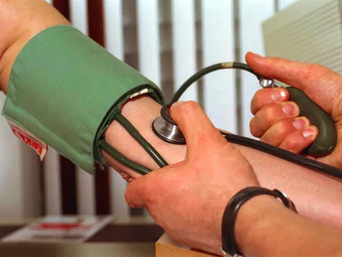 Die Manschette eines mechanischen Blutdruckmessgerätes (Sphygmomanometer) ist um den Oberarm eines Menschen gelegt. Eine zweite Person pumpt die Manschette mit einem Gummiball auf und ermittelt die Druckwerte mit dem Stethoskop.