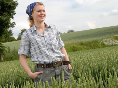 Junge, hemds&auml;rmelige Frau, die in einem Getreidefeld steht, und &uuml;ber das Land blickt