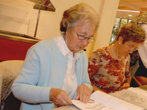 Zwei ältere Damen sitzen an einem Tisch und blättern in Unterlagen.