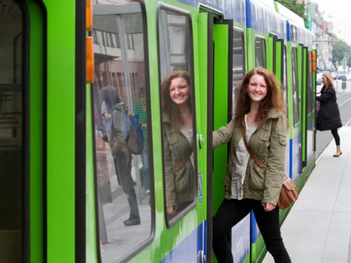 Eine junge Frau steigt in eine Stadtbahn der üstra, ihr Gesicht wird in der Seitenscheibe gespiegelt. Am Fahrzeugkopf steigt eine weitere Person ein.