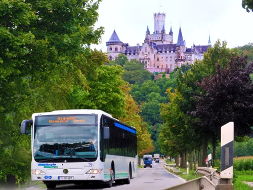 Ein Bus kommt auf einer Landstraße entgegen. Im Hintergrund befindet sich die Marienburg.