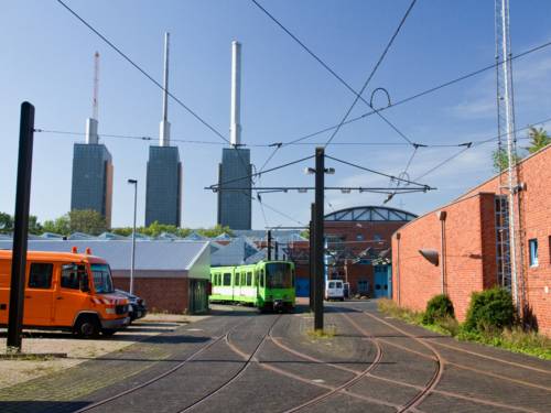 Mehrere Schienenstränge führen zum Betriebshof Glocksee der üstra Hannoversche Verkehrsbetriebe AG, darauf biegt gerade eine grüne Stadtbahn um die Kurve. Im Hintergrund ist das Lindener Kraftwerk zu sehen.