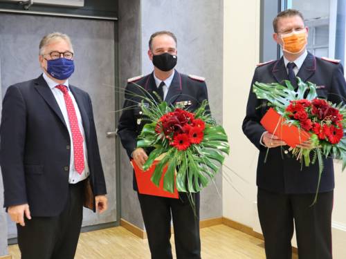 Drei Männer stehen nebeneinander, sie halten Abstand und tragen Mund- Nasen-Bedeckungen. Die zwei Männer neben Regionspräsident Hauke Jagau tragen den Dienstanzug der Freiwilligen Feuerwehr.