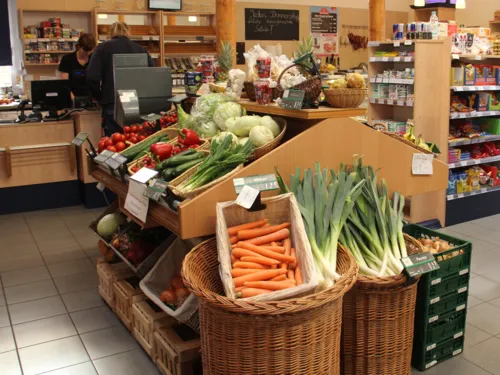 Lauch und Möhren in Holzkisten in einem Laden, im Hintergrund weitere Produkte