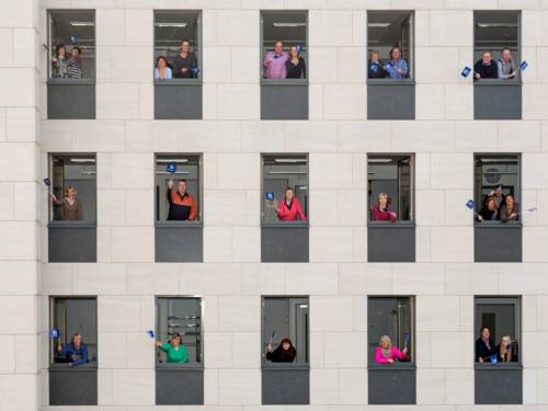 Beschäftigte schauen aus Bürofenstern und schwenken ein Regions-Fähnchen.