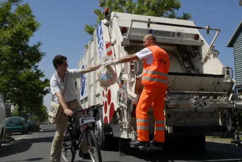 Fahrradfahrer reicht eine Mülltüte einem Mitarbeiter der Müllabfuhr