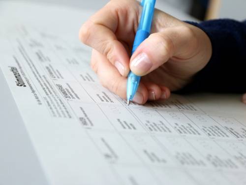 Eine Hand hält einen blauen Kugelschreiber und liegt auf einem Stimmzettel.