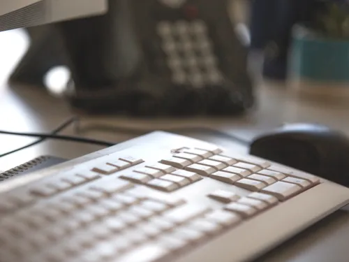 Blick auf ein Telefon, vorbei an einer Computertastatur und Computermaus.
