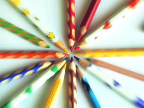 Buntstifte verschiedener Farben liegen auf einen weißen Blatt Papier, durch den Reiss-Zoom-Effekt sind nur die Spitzen scharf.